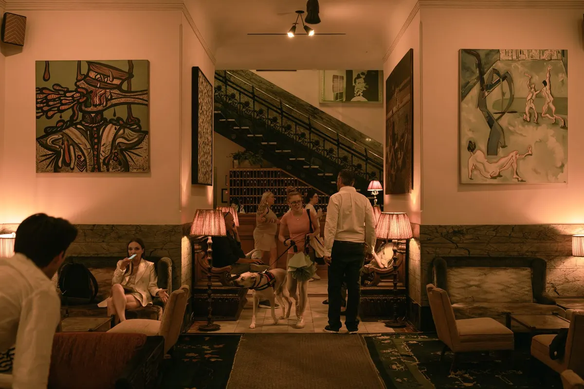 The Chelsea lobby, its staircase and paintings, guests walking through to the bar