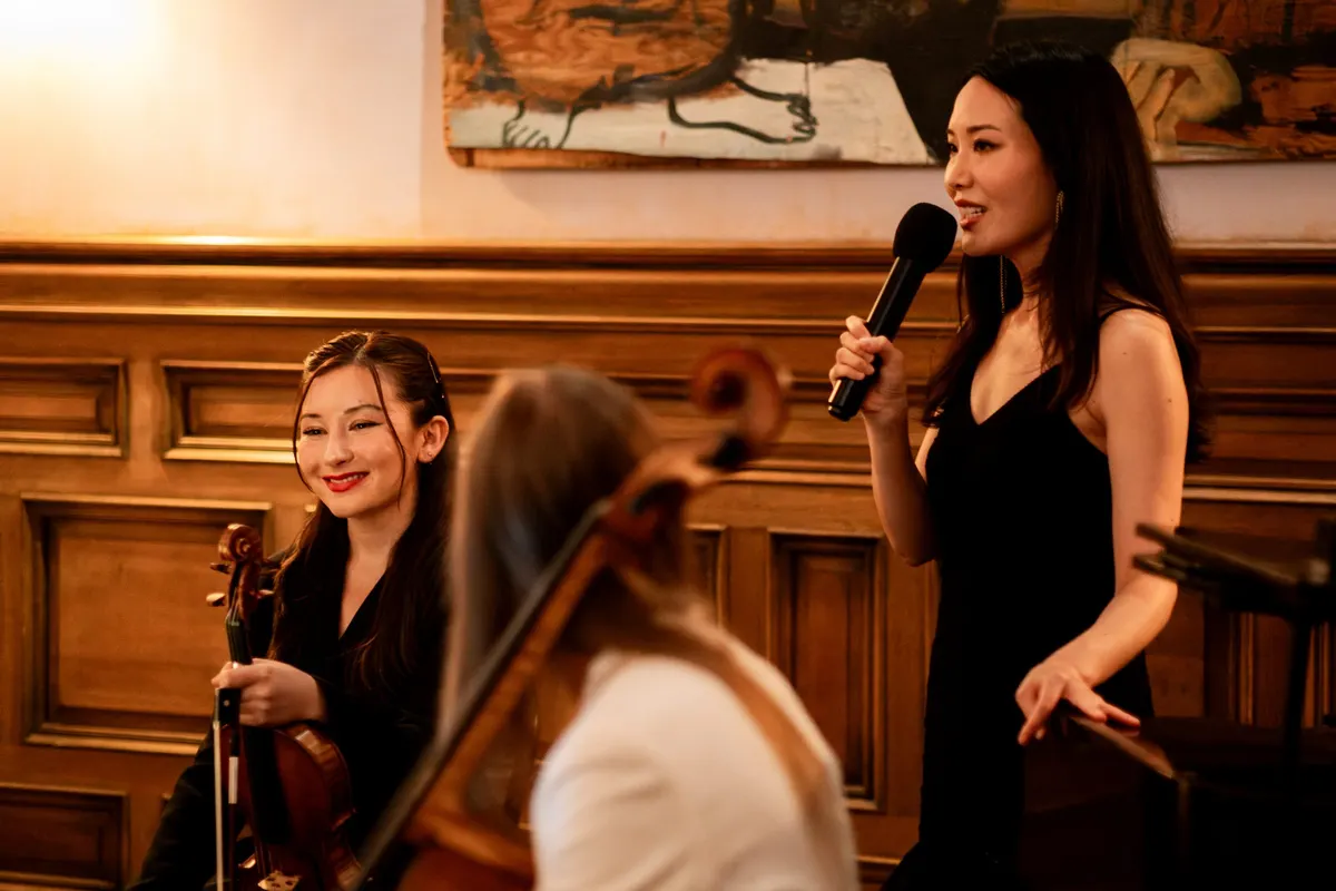 Rieko speaking to the room, Isabelle and Arlen beside her