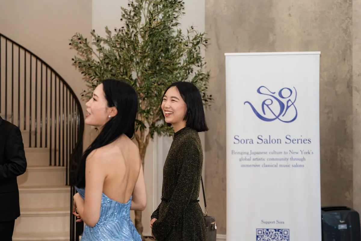 Rieko greeting a guest by the Sora banner at the foot of the stairs